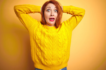 Sticker - Beautiful redhead woman wearing winter sweater standing over isolated yellow background Crazy and scared with hands on head, afraid and surprised of shock with open mouth