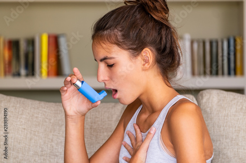 Fotografía young girl having an asthma attack and using an inhaler sitting in a sofa at hom