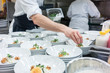 © Kzenon Premium - Hand of a chef styling food in multiple plates in a commercial kitchen with catering services