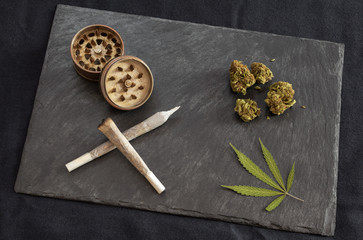 Marijuana joints ready to smoke, high quality cannabis buds, grinder and marijuana leaf in black stone tray. Weed smoking materials, dark background.