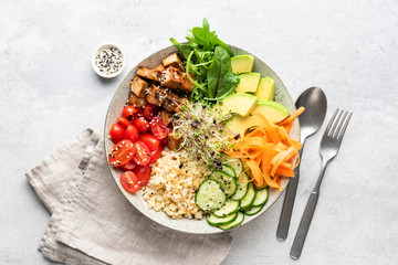 Trendy colorful vegan buddha bowl salad with fried tofu, carrot, cucumber, bulgur avocado tomato and green salad leaf on grey concrete background. Top view. Balanced diet food