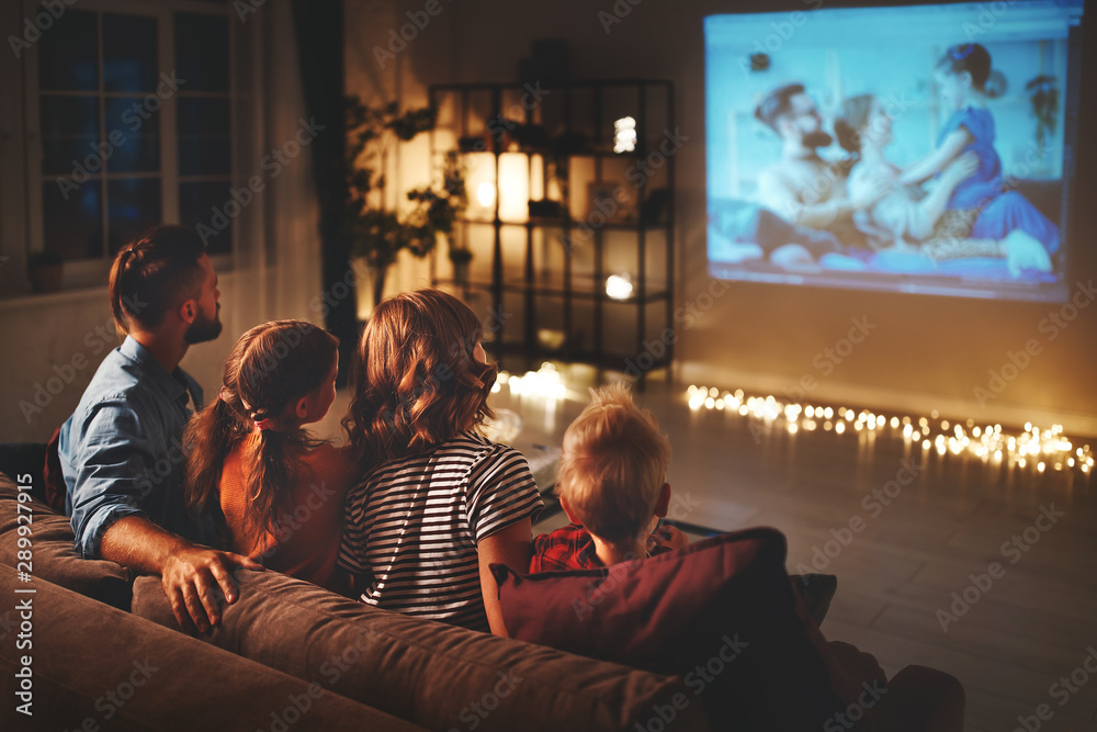 family mother father and children watching projector, TV, movies with popcorn in   evening   at home. - obrazy, fototapety, plakaty 