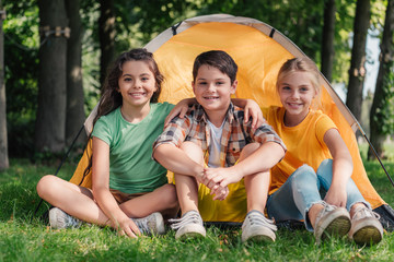 Wall Mural - happy boy sitting with cute friends near camp