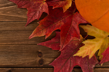 Wall Mural - Pumpkin with red maple leafs disposed on a wooden table. Flat lay, top view of fall autumn concept.