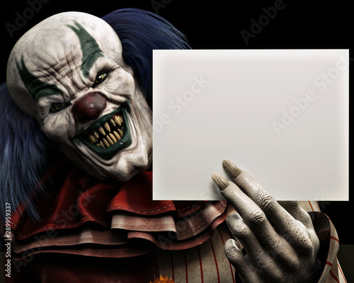 Fotomural Frightening scary clown with sharp fangs piercing the darkness holding a black advertisment card with room for your text or copy space