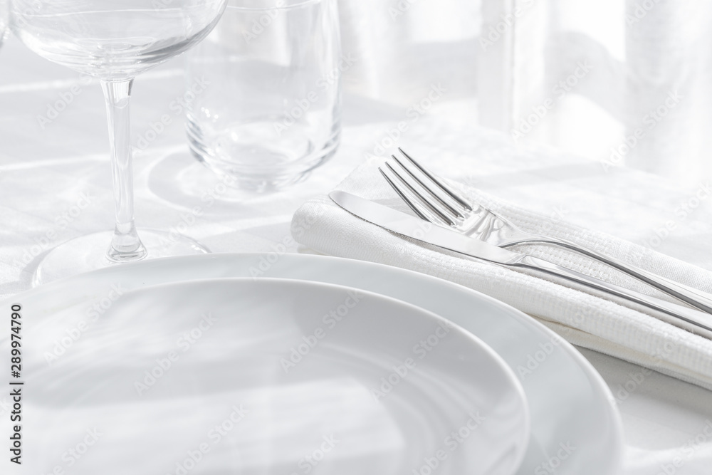 Table setting white and grey colour. Empty glasses and plates set with napkin and cutlery on white table cloth. Restaurant interior background. - obrazy, fototapety, plakaty 