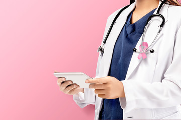 Wall Mural - A woman doctor in a white lab coat with a pink ribbon and a stethoscope holding a tablet with a pink background