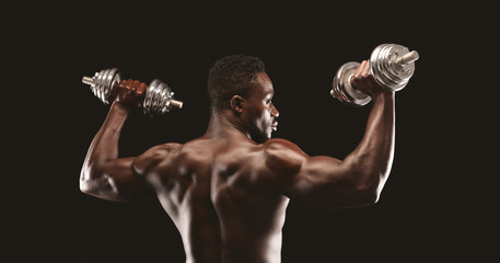 Wall Mural - Strong black guy pumping barbells over black studio background