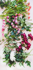 Wall Mural - Various summer flowers flat-lay. Purple peonies, pink roses and tulips, white chrysanthemums and green branches with leaves over pastel pink background, top view, vertical composition