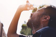 Young man splashing and pouring fresh water from a bottle on his head to refresh against a blue sky background in a summer heat