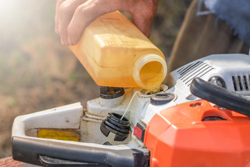 Hand of logger is fueling oil the chainsaw machine close-up.