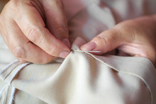 Hand Of The Seamstress Is Using A Needle To Sew Brown Pants By Hand Close-up.