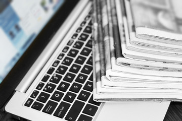 Newspapers and laptop. Pile of daily papers with news on the computer. Pages with headlines, articles folded and stacked on keypad of electronic device. Modern gadget and old journals, focus on paper