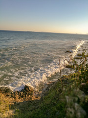 Wall Mural - Waves lapping the rocky shore with dry and green grass and rocks on the horizon