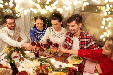 Wall Mural - holidays and celebration concept - happy friends having christmas dinner at home, drinking red wine and clinking glasses