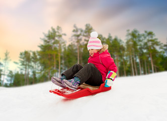 Sticker - childhood, sledging and season concept - happy little girl sliding down on sled outdoors over winter forest background