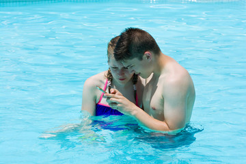 Canvas Print - Teenage girl and boy watching pictures on smartphone taken during photo shoot in luxury hotel swimming pool. Summer vacation concept