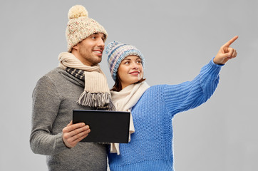 Canvas Print - technology, christmas and winter clothes concept - happy couple in knitted hats and scarves with tablet computer over grey background