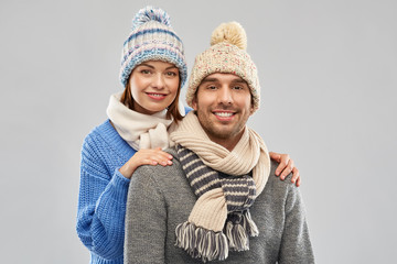 Sticker - people, christmas and winter clothes concept - happy couple in knitted hats and scarves over grey background