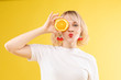 © Вячеслав Косько - Stock photo of positive blonde young woman in white t-shirt with halved orange holding it in front of her eye and pouting lips at camera. Isolate on yellow background. Summer concept.
