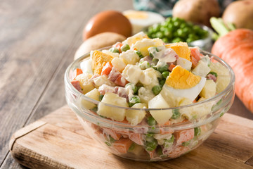 Traditional Russian salad and ingredients for Christmas. Olivier salad on wooden table. 