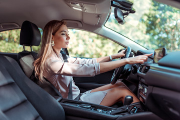 Business girl in summer city, sitting in car, hand selects mode on touch screen display, route selection, enabling functions, automatic transmission, pink suit, traffic jam in background trees.