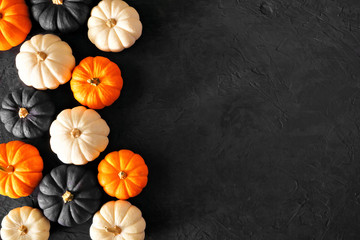 Autumn pumpkin side border in Halloween colors orange, black and white against a black stone background. Copy space.