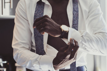 Sexy confident male in opened white shirt is putting cufflink on his cuff.