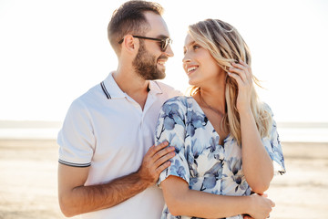 Wall Mural - photo of beautiful happy couple smiling each other and hugging while walking on sunny beach