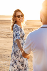 Sticker - Photo of happy beautiful couple smiling and holding hands together while walking on sunny beach