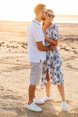 Sticker - Photo of happy young couple smiling and hugging while walking on sunny beach