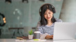 © Songsak C - Young women using laptop and listening song in on-ear headphones.