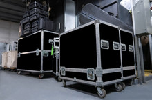 Several Large Black Road Cases Organized In A Corner Of A Back Storage Room With Equipment Cases Stacked On Top.