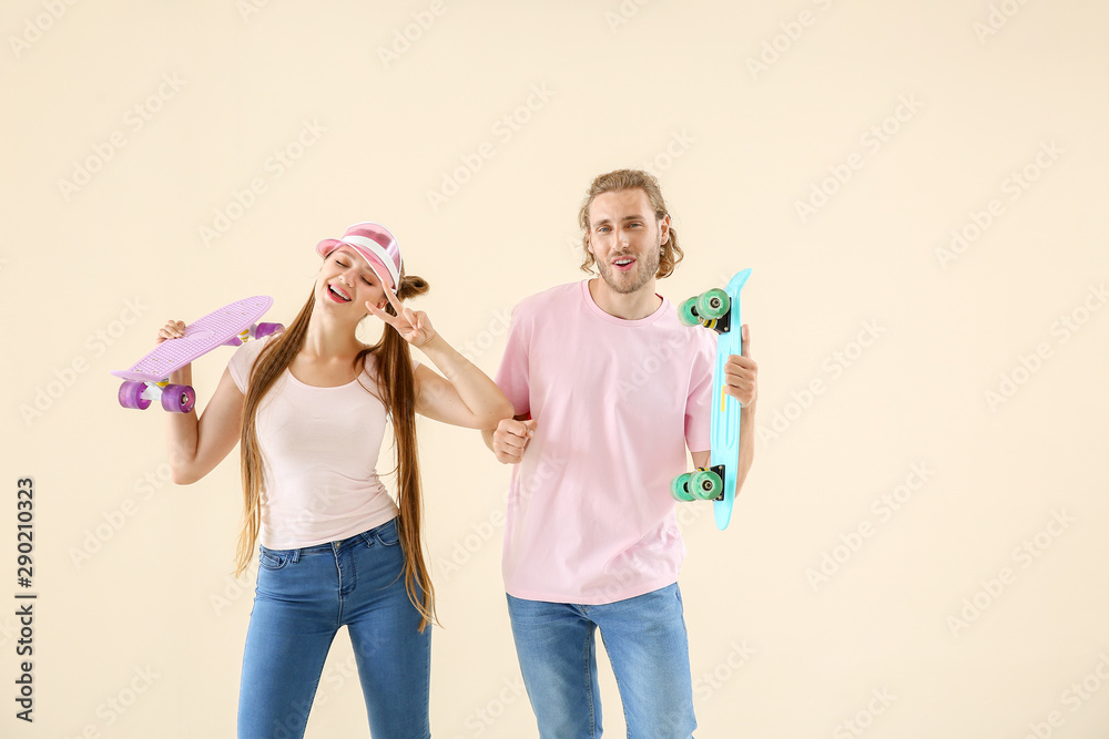 Cool young couple with skateboards dancing against light background