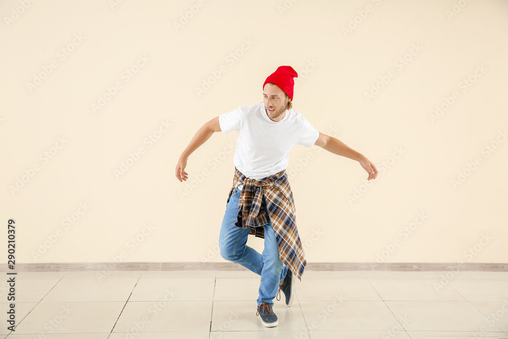 Cool young man dancing against light wall