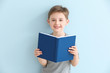Little boy reading book on color background