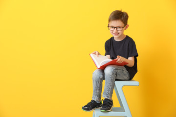 Little boy reading book on color background