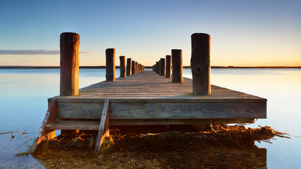 Wall Mural - Calm Lake with symmetrical wooden Pier in the Warm Light of the Rising Sun
