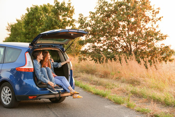 Wall Mural - Happy couple sitting in trunk of their new car in countryside