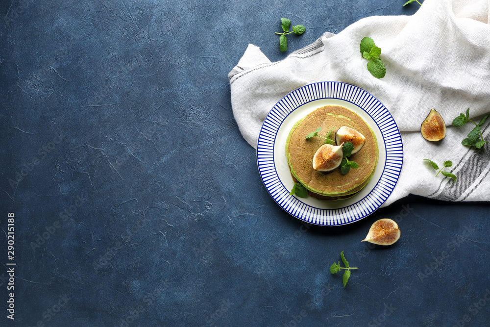 Plate with green pancakes and fig fruit on color background