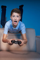 Wall Mural - Excited boy lying on sofa back playing video game with joystick