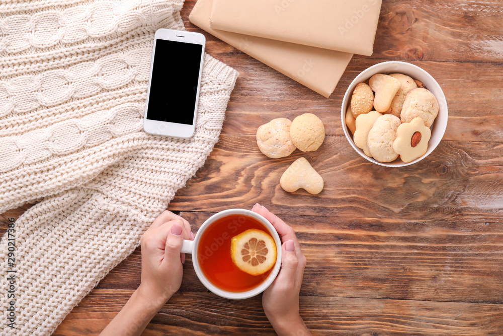 Young woman drinking hot tea and eating cookies at table