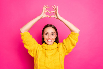 Wall Mural - Portrait of cheerful lady makiing heart from her fingers smiling wearing yellow sweater isolated over fuchsia background