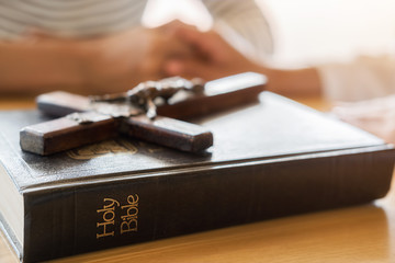 Wall Mural - Christian woman praying with hands together on holy bible and wooden cross. Woman pray for god blessing to wishing have a better life and believe in goodness.