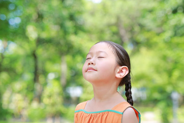 Wall Mural - Portrait of happy Asian child close their eyes in garden with Breathe fresh air from nature. Close up kid girl relax in green park for good health.