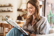 © Drobot Dean - Positive optimistic redhead woman indoors sitting at home reading book or magazine.