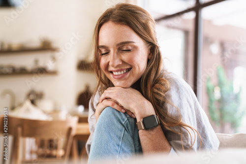 Cuadros en Lienzo Smiling happy redhead woman indoors sitting at the kitchen at home