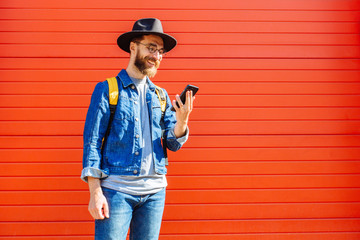 young handsome bearded hipster man using smartphone and listening music with earphones in the city, headphones, sunglasses street, outdoor portrait, cap, hat, concept, hipster male, wall