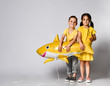 © FAB.1 - Positive little children, dressed in festive clothes, wears a balloon in the shape of a yellow shark fish, celebrates a holiday, has a wide smile, stands on a light background, being in a good mood.