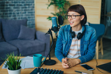 Joyful young woman is talking in professional microphone sitting at table in recording studio working alone. Happiness, emotions and occupation concept.